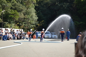 屋外で長く延びたホースの先を手に持った人が放水をしている写真