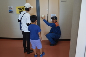 屋内の部屋の前の扉に男性が手をかけておりそれを子どもと大人が見ている写真