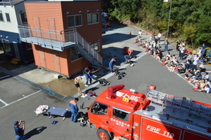 大きな消防車の前で人が作業しているのを奥の多くの人たちが観ている写真