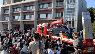 赤い車両の上にいる男性の周りに多くの人たちが集まっている写真