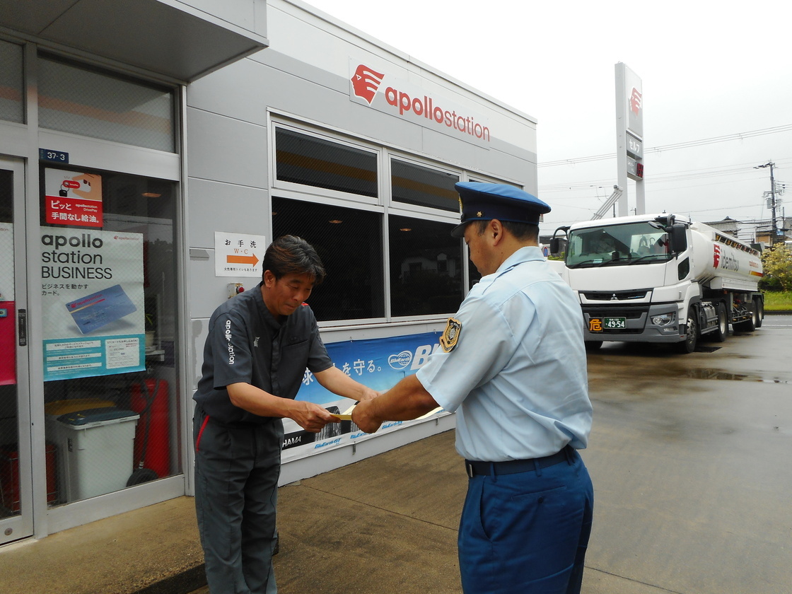 給油取扱所の建物前で、消防職員から表彰状を受け取る写真