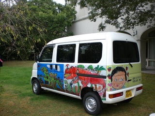 横と後ろの車体にラッピングがされている小型の商用バンを後ろから撮影した写真