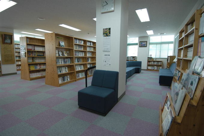 本が沢山置かれた本棚と、紺色のソファが置かれた紫と灰色の格子状の床がある室内の写真