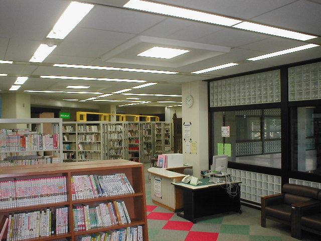 壁に時計がかかっており、ガラス窓があり、数多くの本が並んでいる本棚が沢山並んでる室内の写真