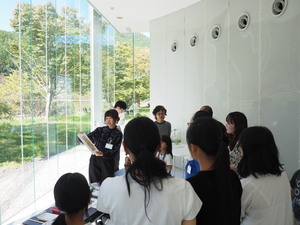 太陽の降り注ぐガラス張りの部屋で講師の説明に耳を傾けるワークショップの参加者たちの写真