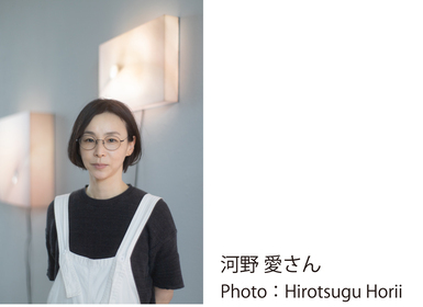 黒いTシャツの上に白いサスペンダーを着て自作の前に立つ、講師の河野 愛さんの写真 Photo：Hirotsugu Horii