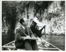 スーツを着て小船に腰掛ける渡瀬凌雲と、小船を漕ぐ男性が写った白黒写真