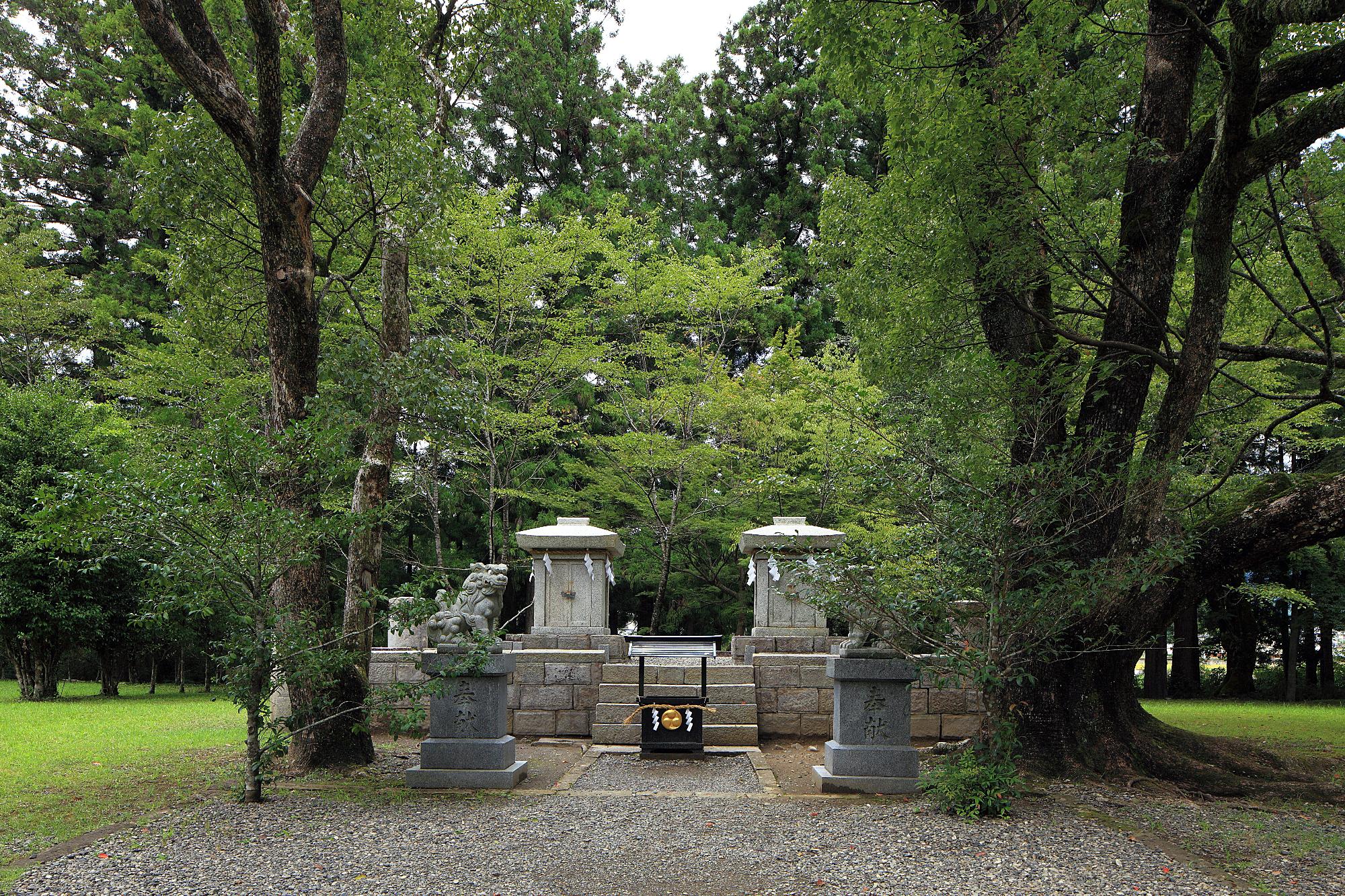 中央に石造の小祠が建てられ、周りを木々が取り囲んでいる場所の写真
