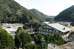 山間の場所に多くの旅館や温泉施設が立ち並ぶ温泉街を山側から撮影した写真