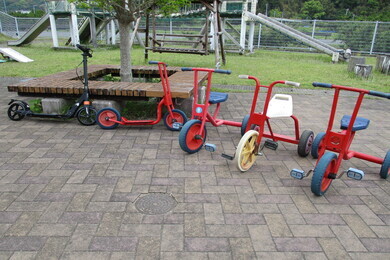 赤い三輪車と黒と赤いキックボードが並んでいる写真