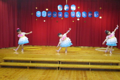 ステージの上でリボンと水色の縁がついたドレスを着た3人の女の子がポーズをとっている写真