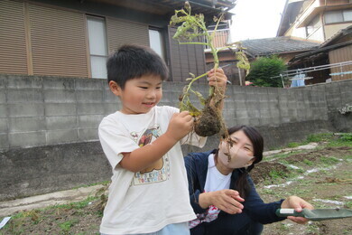 一人の園児が収穫した野菜を見ながら職員さんも一緒に喜んでいる写真
