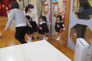 制服を着た女の子の園児がドアをくぐったあと大人に手を引かれている写真