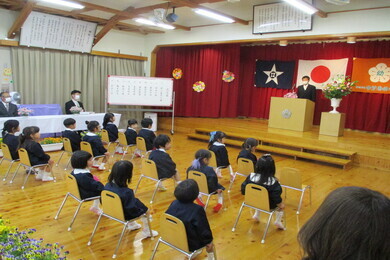 体育館のような場所に椅子が並べられ制服を着た園児たちが座っている写真