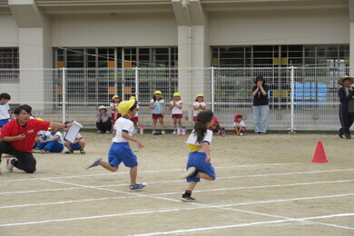 スポーツテストに取り組んでいる小学生たちの近くで見学をしている園児たちの写真