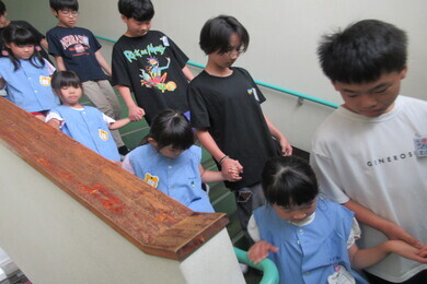 幼児たちが小学校で6年生に手を繋がれて階段を下りている写真