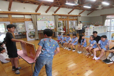 園児たちが椅子に座りながら小学生の絵本の読み聞かせを聞いている正面からの写真
