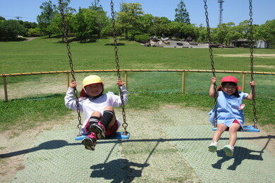 帽子を被った女の子の園児二人がブランコに乗っている写真