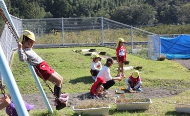 園児たちがブランコや砂場で楽しそうに遊んでいる写真
