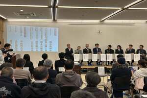 前方の演壇に1列に並んだ人と、それに向かい合う形で数列に分かれて着席している参加者たちの写真