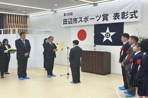 スポーツ賞表彰式にて、マイクの前に立つ男性から表彰状を授与されている写真