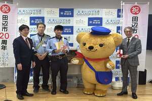 左に3人の男性、くまの着ぐるみを着た人、グレーのスーツの方が並び、記念写真をとっている写真