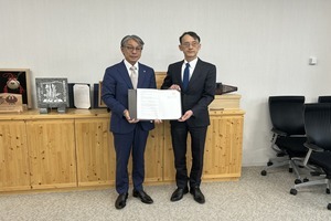 スーツ姿の男性二人が、並んで協定書を手に持ち、正面を向いて記念撮影をしている写真