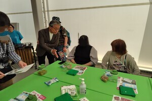 緑色のテーブルに座っている2人の女性に対し、スーツ姿の男性が親しげに話しかけている写真