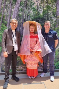 木々の緑が背景に、着物を着た女性を中央、その両サイドにスーツを着た男性2人が挟む形で、3人で並んでいる写真