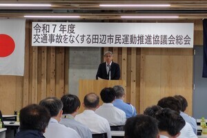 スーツ姿の男性がマイクの前に立ち、出席者に向けて話をしている写真