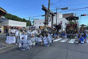 笠鉾の周囲に法被を着た大勢の参加者たちが地面に座っている写真