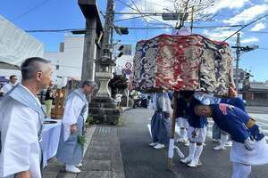 法被を着た男性が1人立っており、その前方で同じく法被姿の男性たちの集団がお辞儀をしている写真