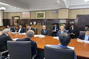 会議室のテーブルにて、スーツ姿の男性たちが対面形式で座り、資料を前に協議を行っている写真