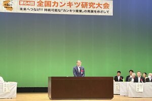 ホールのステージ上でスーツ姿の男性が話をしている写真