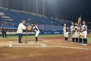 球場で選手たちが横一列に整列し、代表の選手が前方に立つ男性から賞状などを受け取っている写真