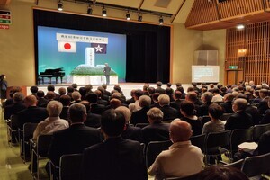 ホールの前方に祭壇があり、客席には多くの参加者が座っている写真