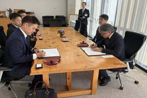 機のテーブルの上に置かれた書状にサインをしている男性たちの写真