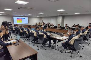 広い会議室で机に置かれた紙を見る人たちの写真