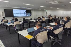 大きなモニターを見ながら机に座っている人たちの写真