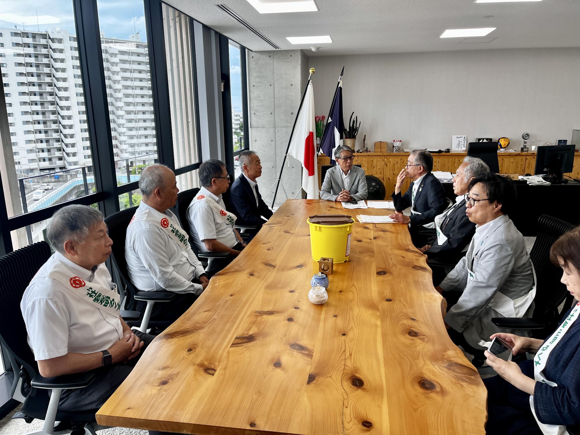 会議机に男女数名が席についてお互い向かい合いながら話しをしている写真