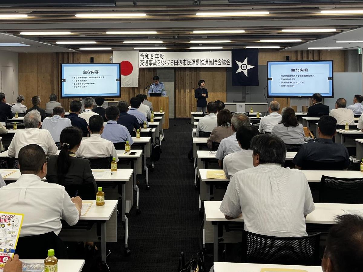 会議室で人が、並べられた机と椅子があり、座って話を聞いている写真