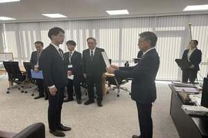 左側の男性が、右側の眼鏡をかけた白髪の男性から書類を受け取っている着任式の写真