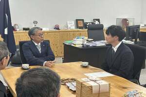 デスクにて、数人の男性たちが座り、手元の資料を見ながら対面で話し合いを行っている写真