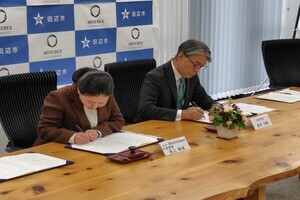 壁一面に本棚がある室内で前方モニター画面を使って説明を行っている人物と、その前で話を聞いている写真