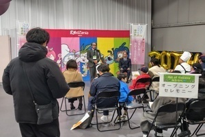 会議室の前方に立った人が資料を提示し、その前に大勢の参加者が席に座って話を聞いている写真