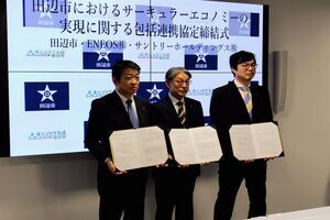 画面が映し出されているモニターの前で、3人の男性が手に資料をもって並んでいる写真