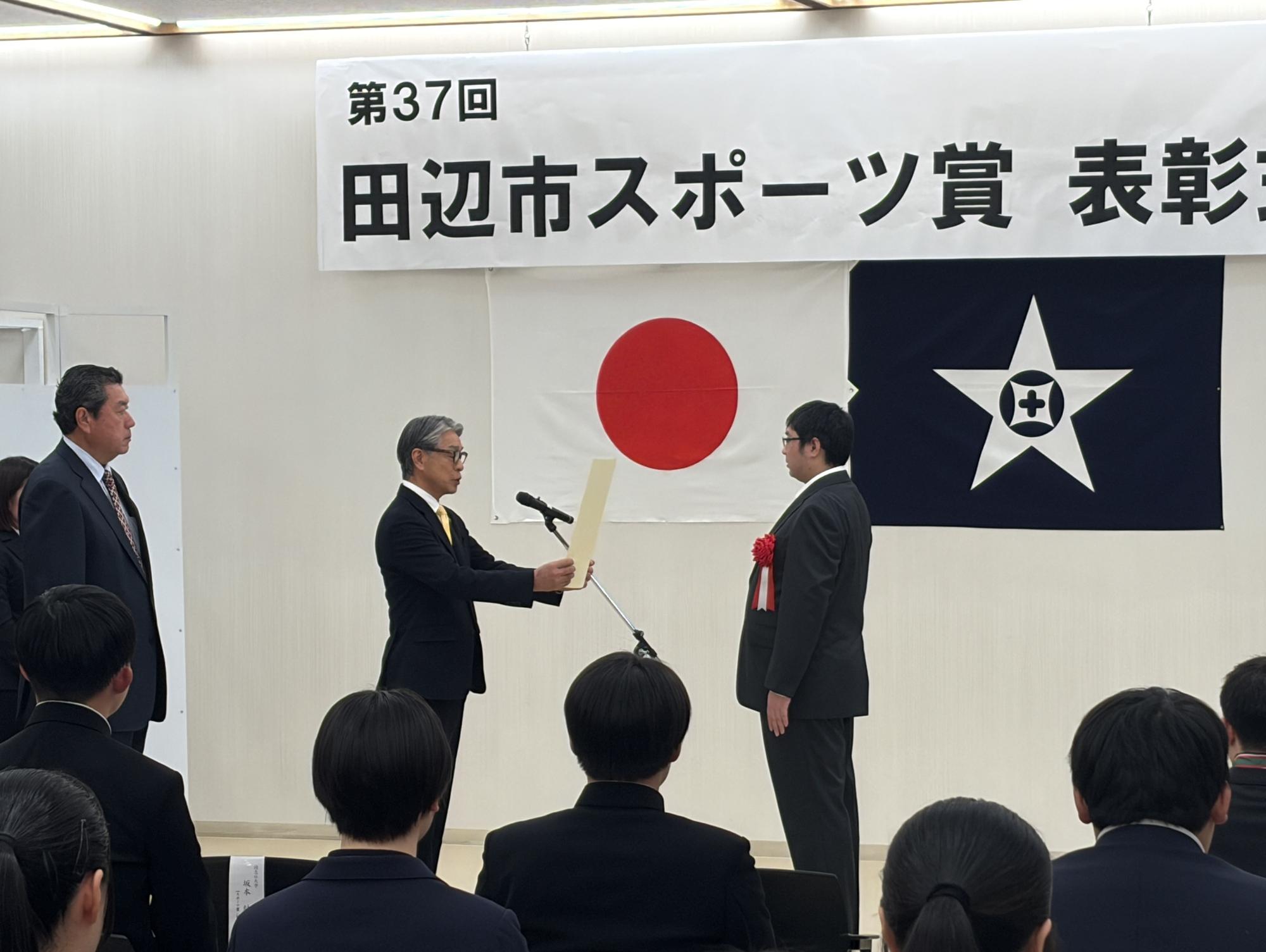 スポーツ賞表彰式にて、マイクの前に立つ市長から表彰状を授与されている写真