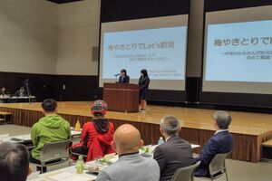 ステージの壇上に2人の女性が立ち、マイクを前にして並んで発表を行っている写真