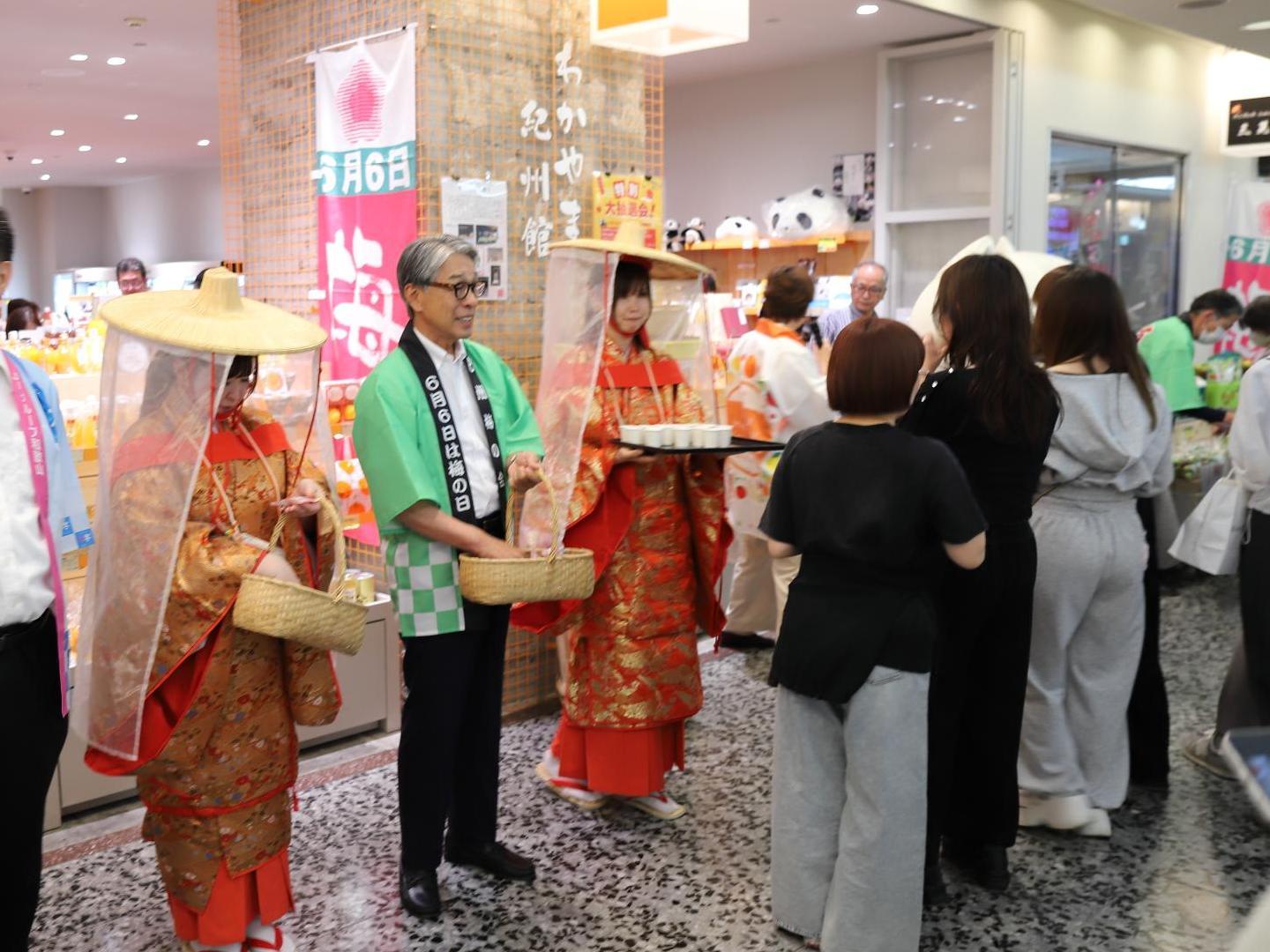 会場内に集まった大勢の人たちが、展示物を見たり、黄緑の法被の男性から何かを受け取っている写真