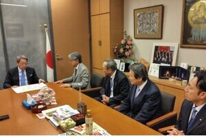 男性がマイクを手に持ち、前方に立つスーツ姿の男性へ向けて質問をしている写真